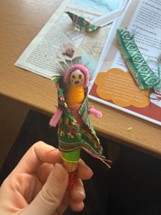 A small peg doll wearing colouring fabric.