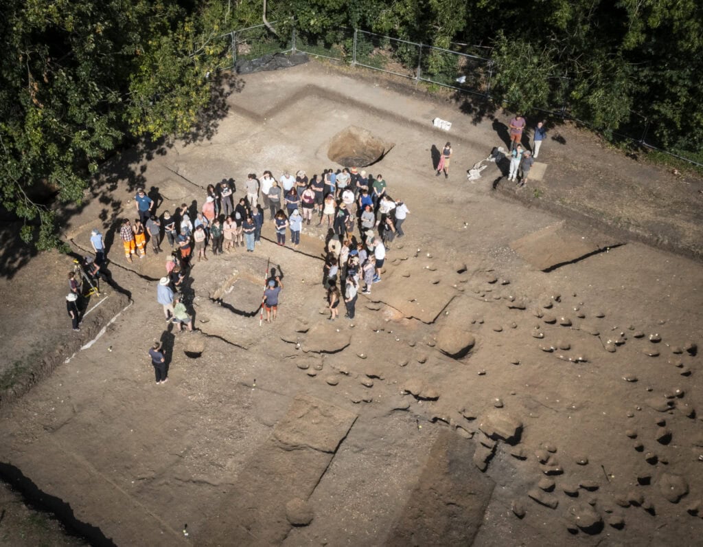 An aerial view of an archaeological dig site where a large group are on a guided tour.