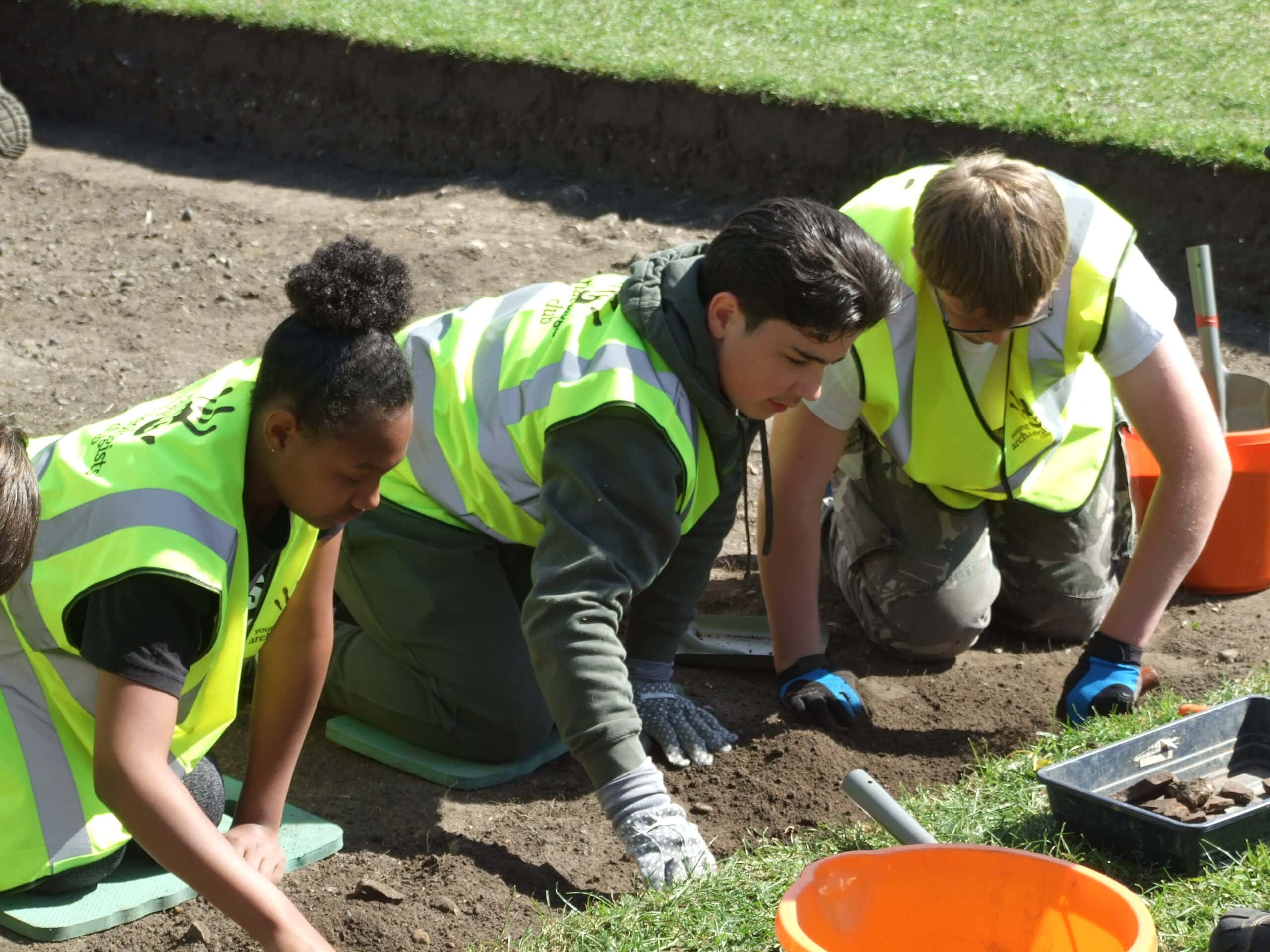 Three young people digging in an archaeological excavation