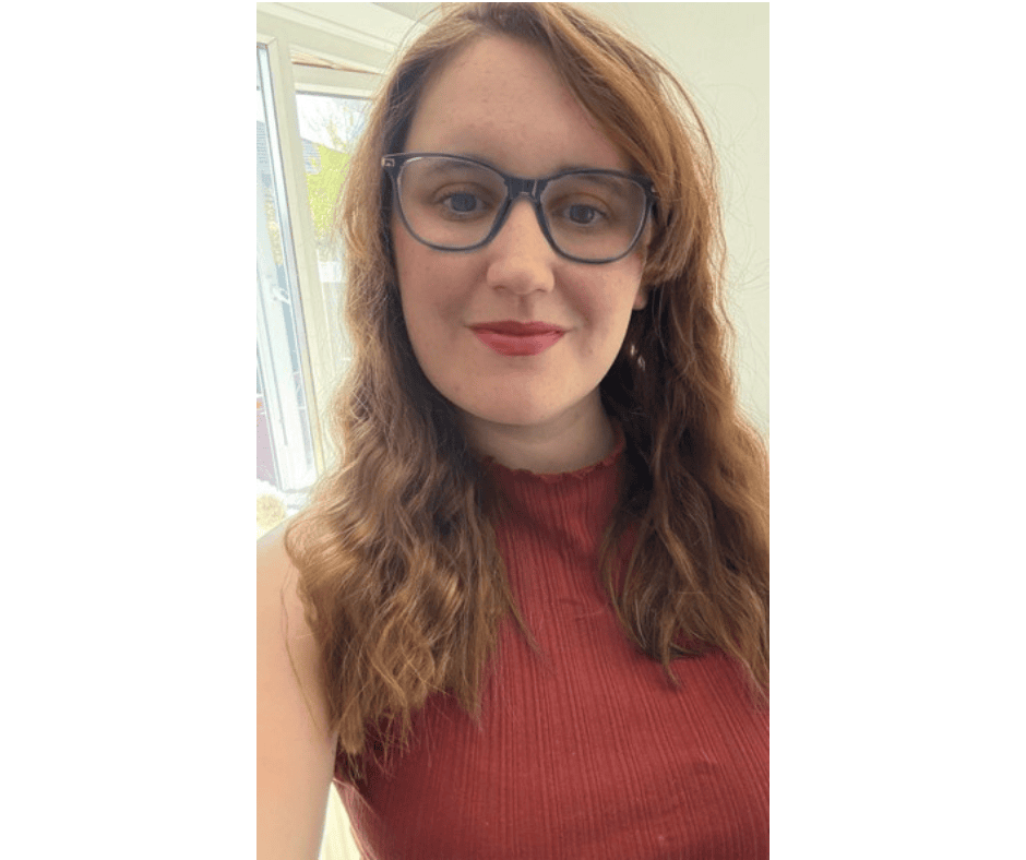 A woman with shoulder length red-brown hair wearing glasses and a red top