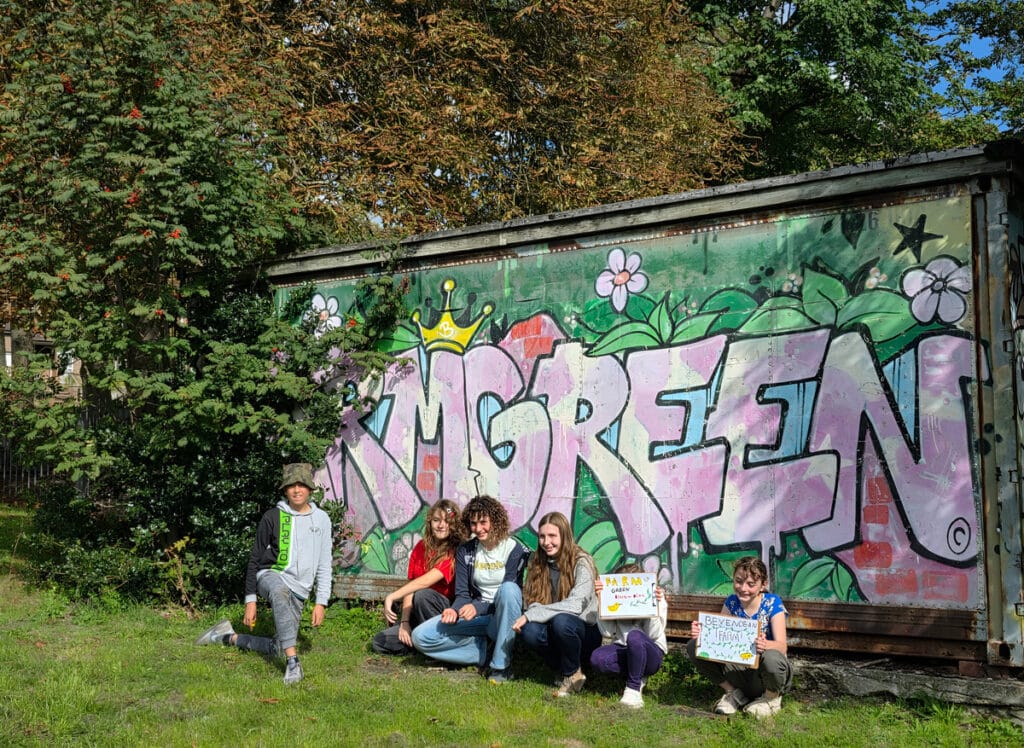six young people crouched in front of graffiti sign saying FarmGreen
