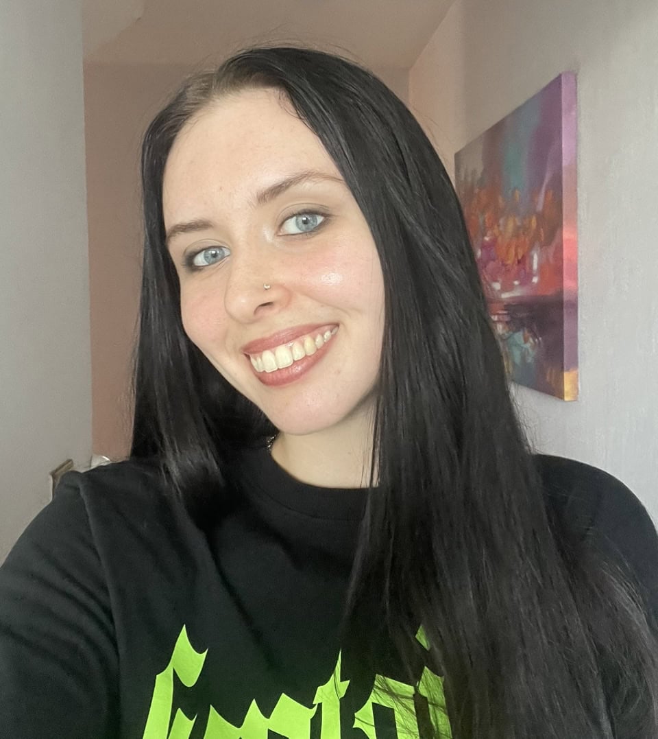 Photo of Emily smiling with long black hair and black top with lime green writing