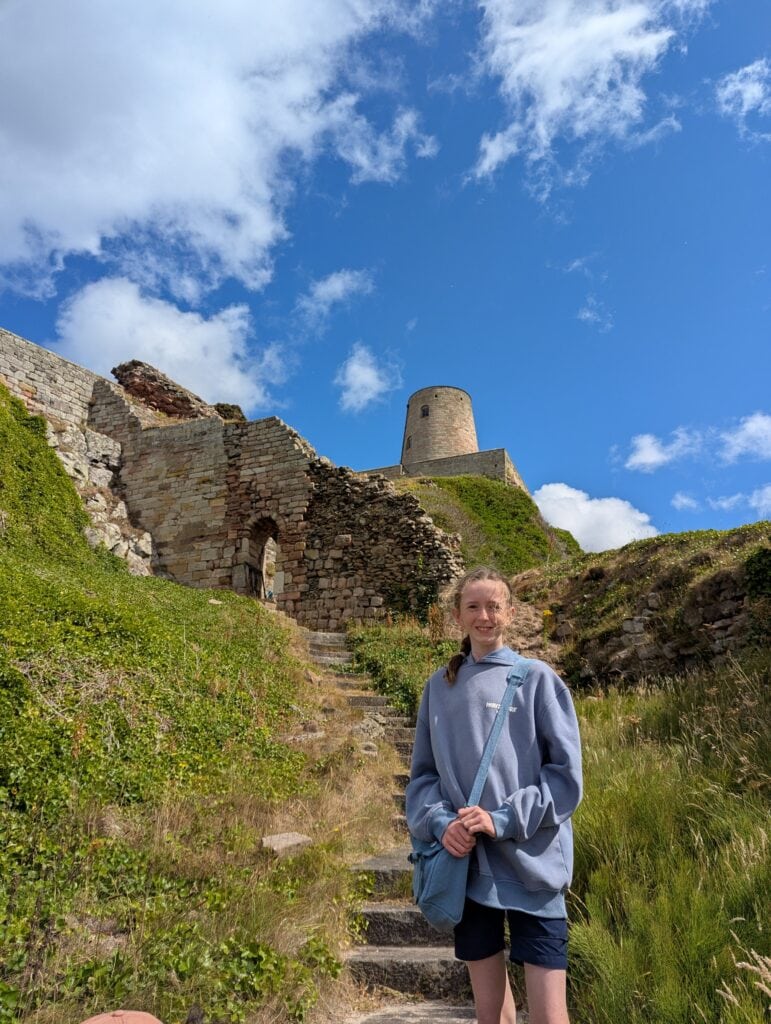 A young person stood in front of a medieval castle on a sunny day.